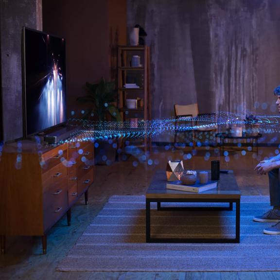 Man in a living room watching TV with sound waves radiating from the speaker system showing the effects of Dolby Atmos
