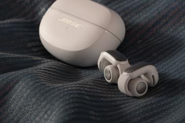 Bose Ultra Open Earbuds and charging case on a blanket.